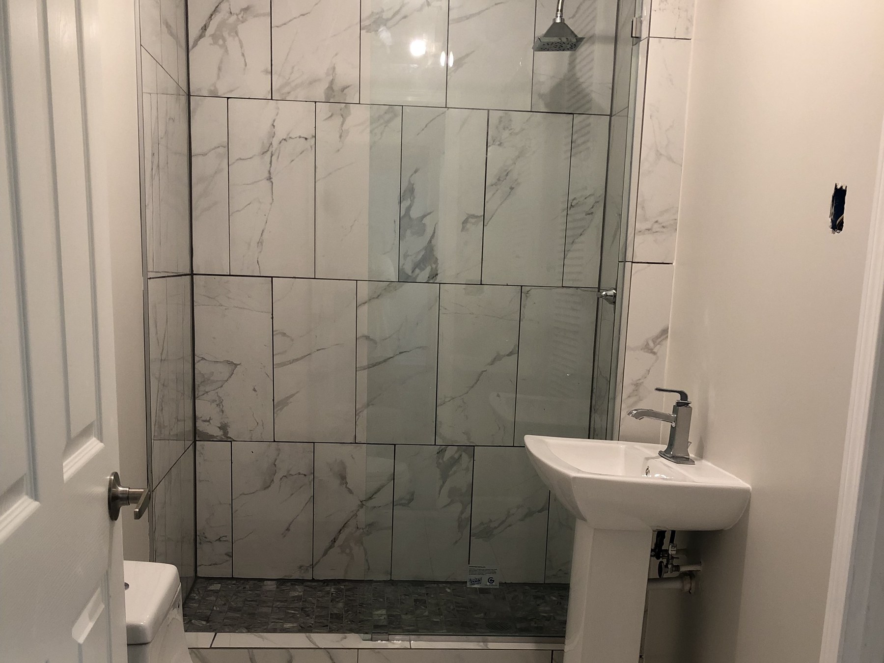 Finished bathroom with marble tile shower, glass door, and white fixtures